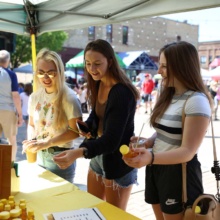 3-Girls-at-the-farmers-market-buying-honey 3 girls looking at a honey vendor while shopping at the downtown farmers market in Grand Forks