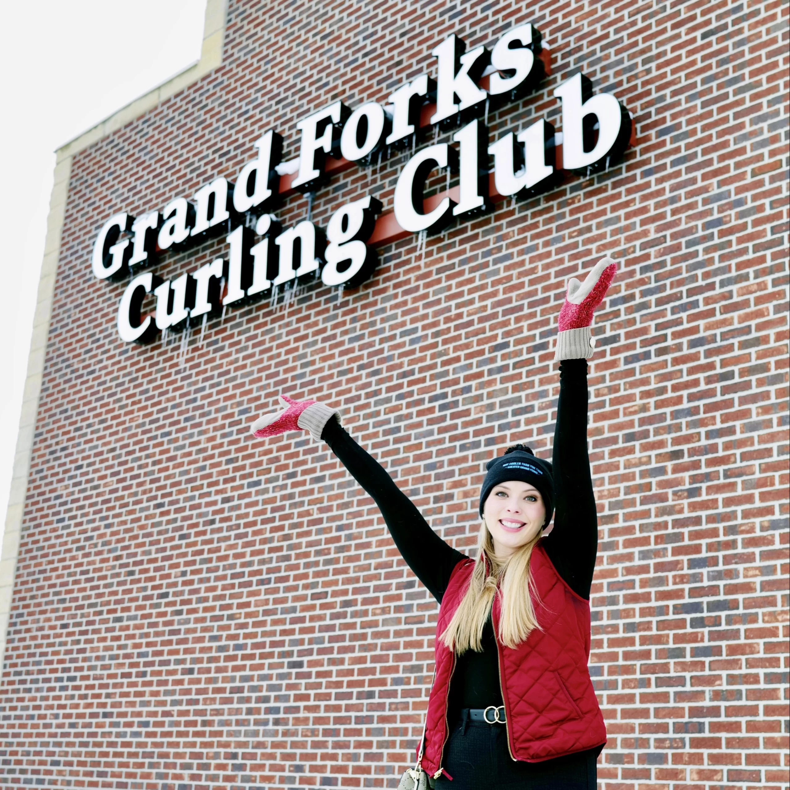 winter-in-grand-forks-curling Winter in Grand Forks Cassandra standing in front of brick building that reads, 'Grand Forks curling club'