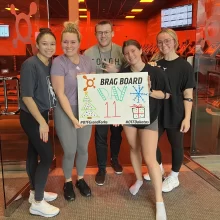 Orange-Theory 5 people stand with the Orange Theory 'brag board' that reads 'day 11' in Grand Forks.