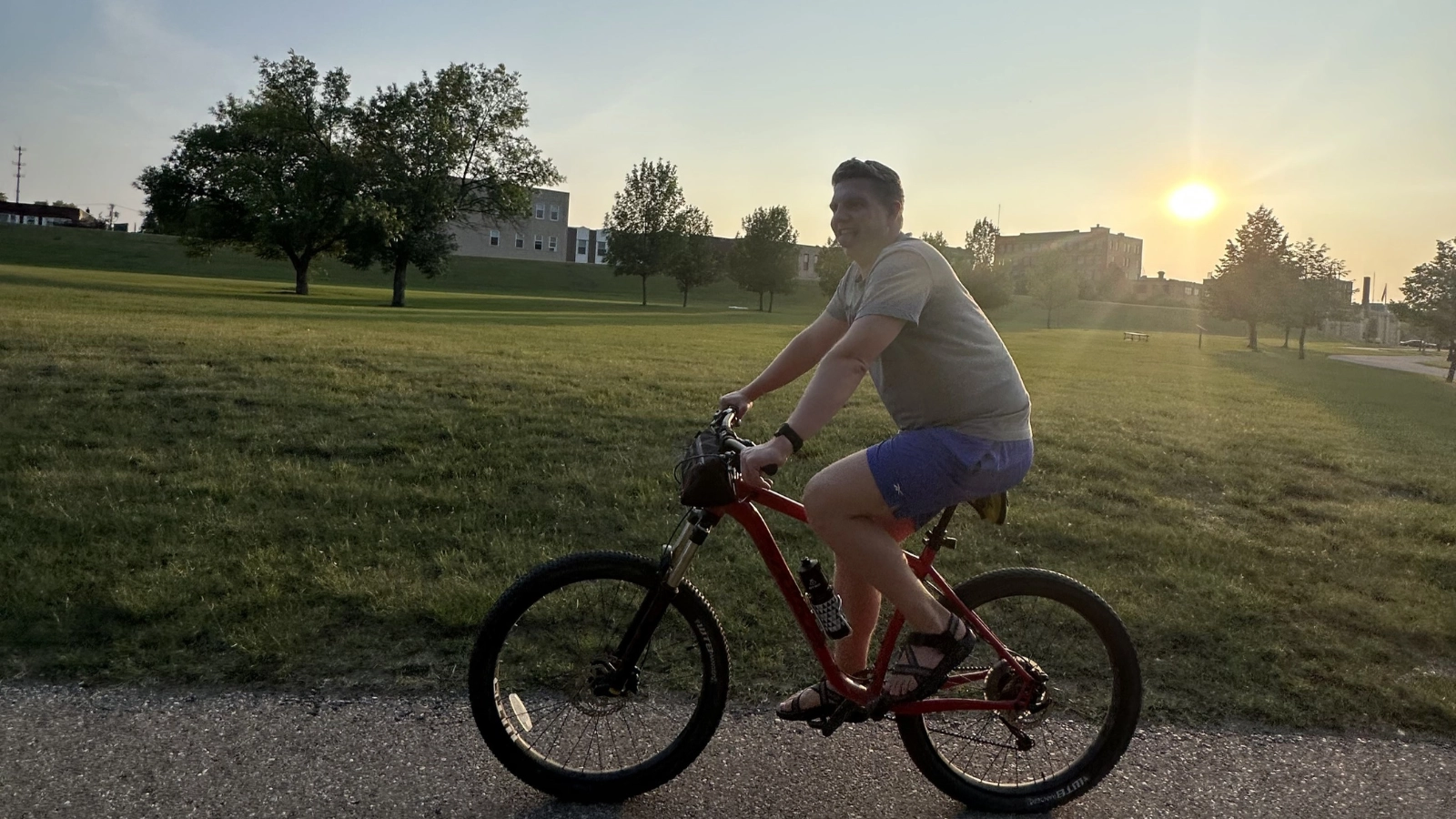 WCT author Paul makes a silly face while riding his bike down the Greenway. A sunset over a school in the back.