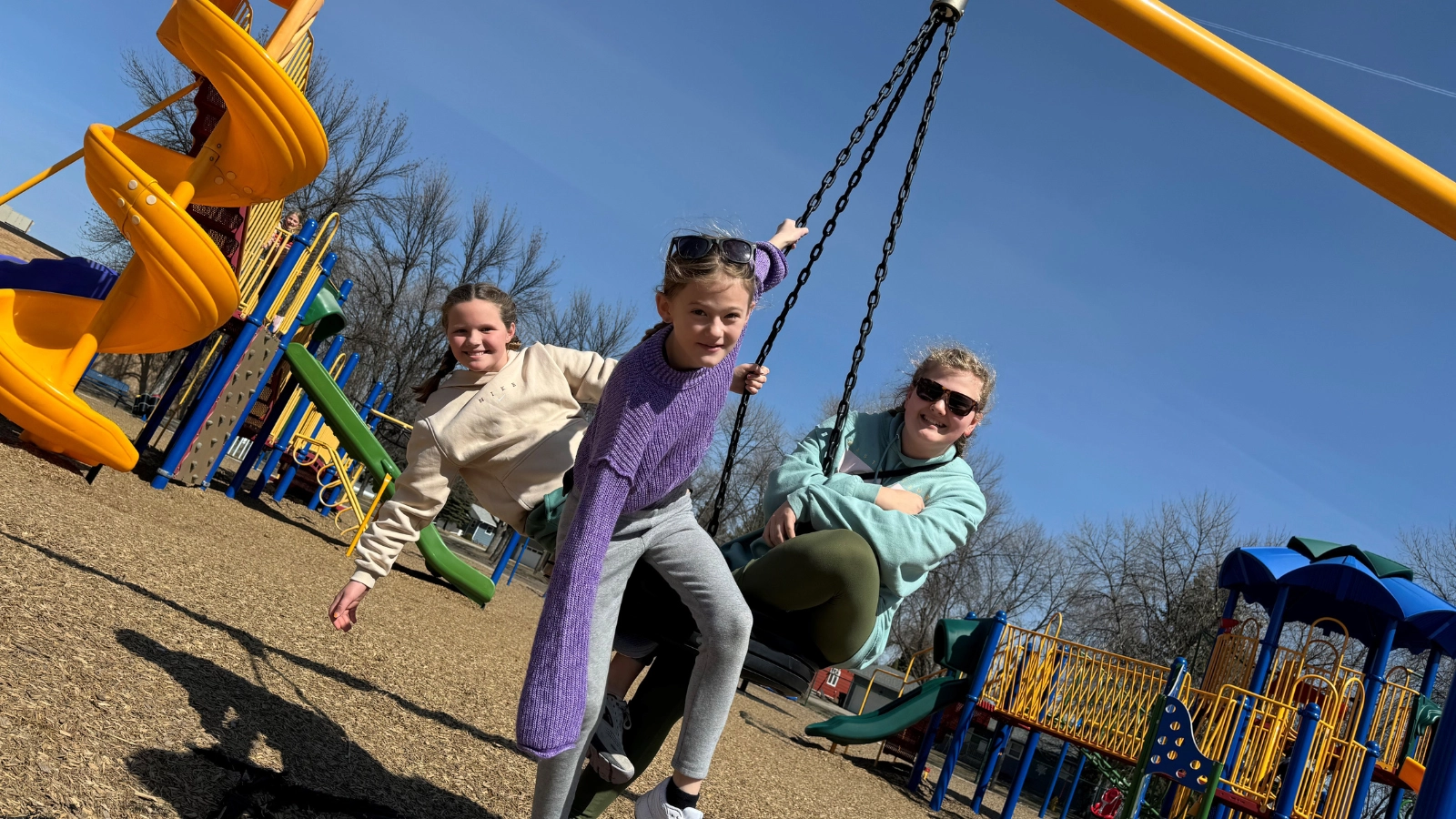 swing-park Three girls play on a tire swing at the park with slide in view.