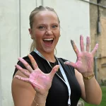 Author Isabelle poses in front of the camera with a big smile on her face. She is holding up both hands that are covered in pink paint.
