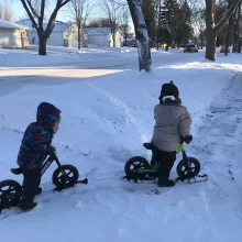 Two Kids biking Author Lacey's kiddos snow biking along on the sidewalk in a bunch of snow!