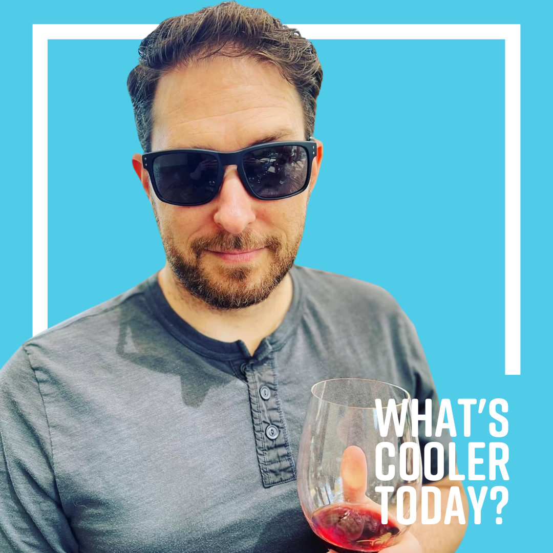 Author Ben poses for his headshot holding near empty wine glass and smiling faintly at the camera while wearing sunglasses.