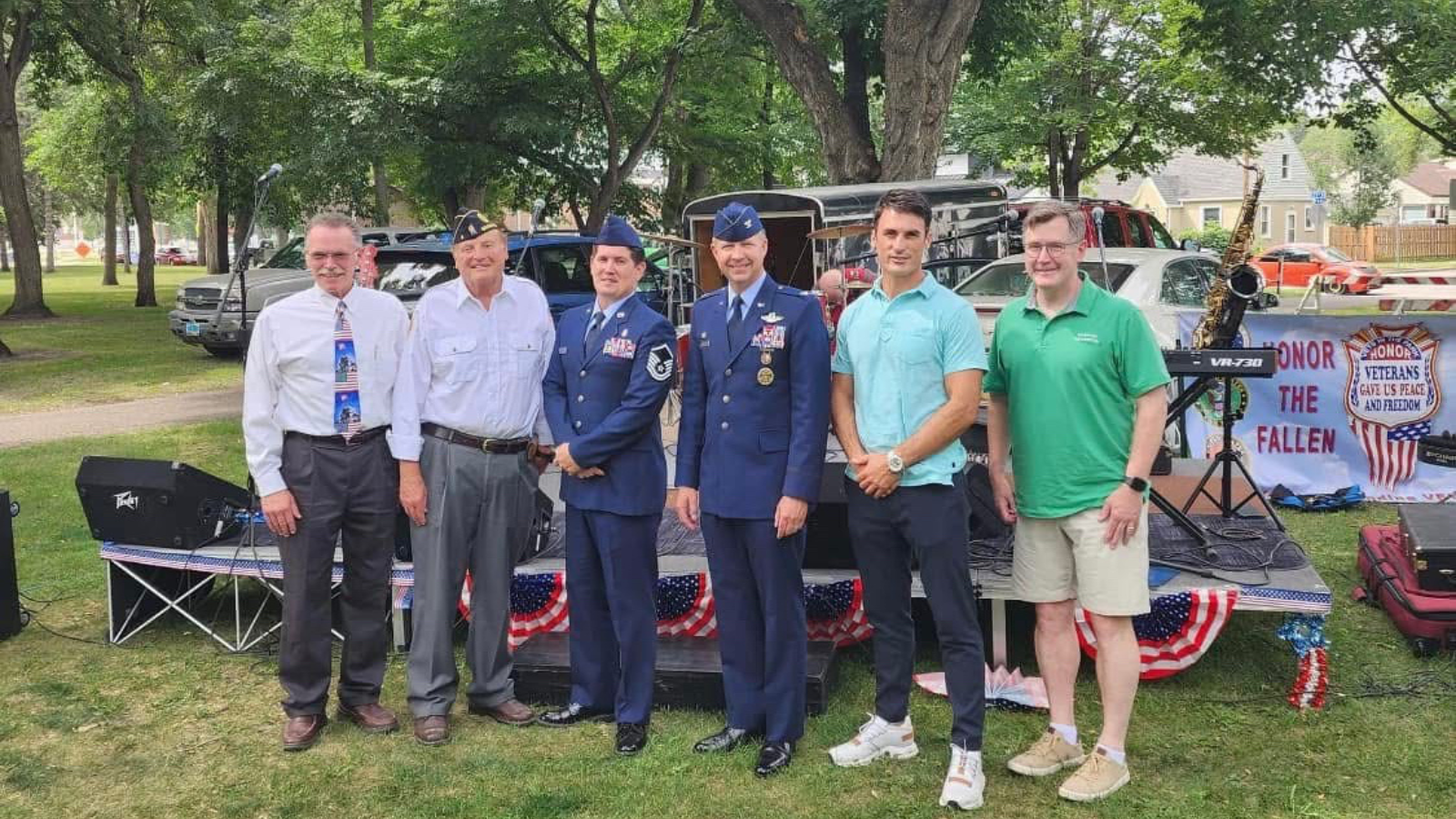 Author Bru is pictured alongside other military and community members in a lineup of six people. He stands third from the left in his uniform standing proudly.
