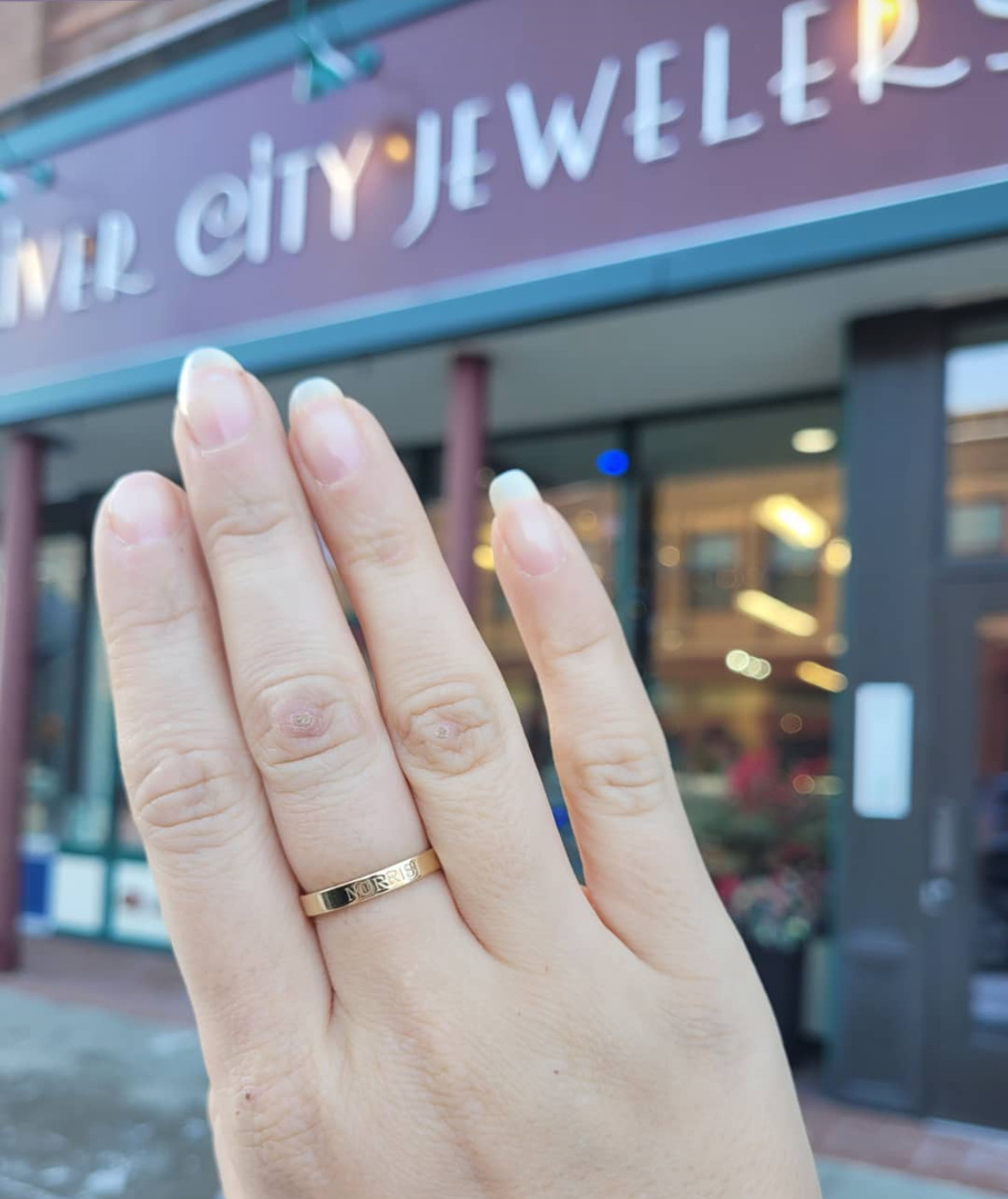 Pictured is the authors hand wearing a River City Jewelers "mother" themed ring. She holds up her hand wearing the ring in front of the store.