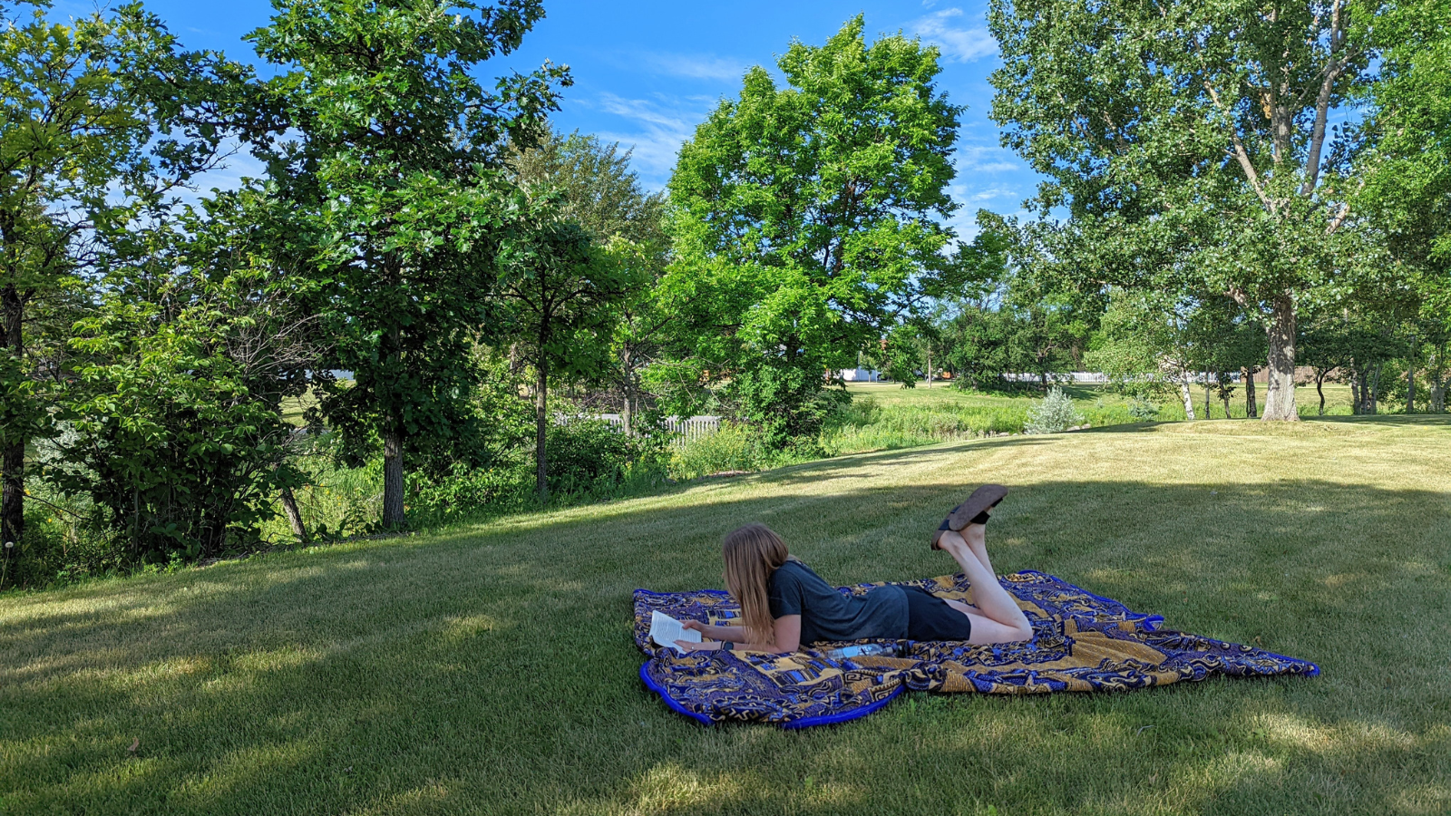 Grand Forks resident lays in the grass at a lovely Grand Forks park to relax and read.