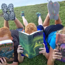 Three summer readers face the camera with their Harry Potter books covering their faces.