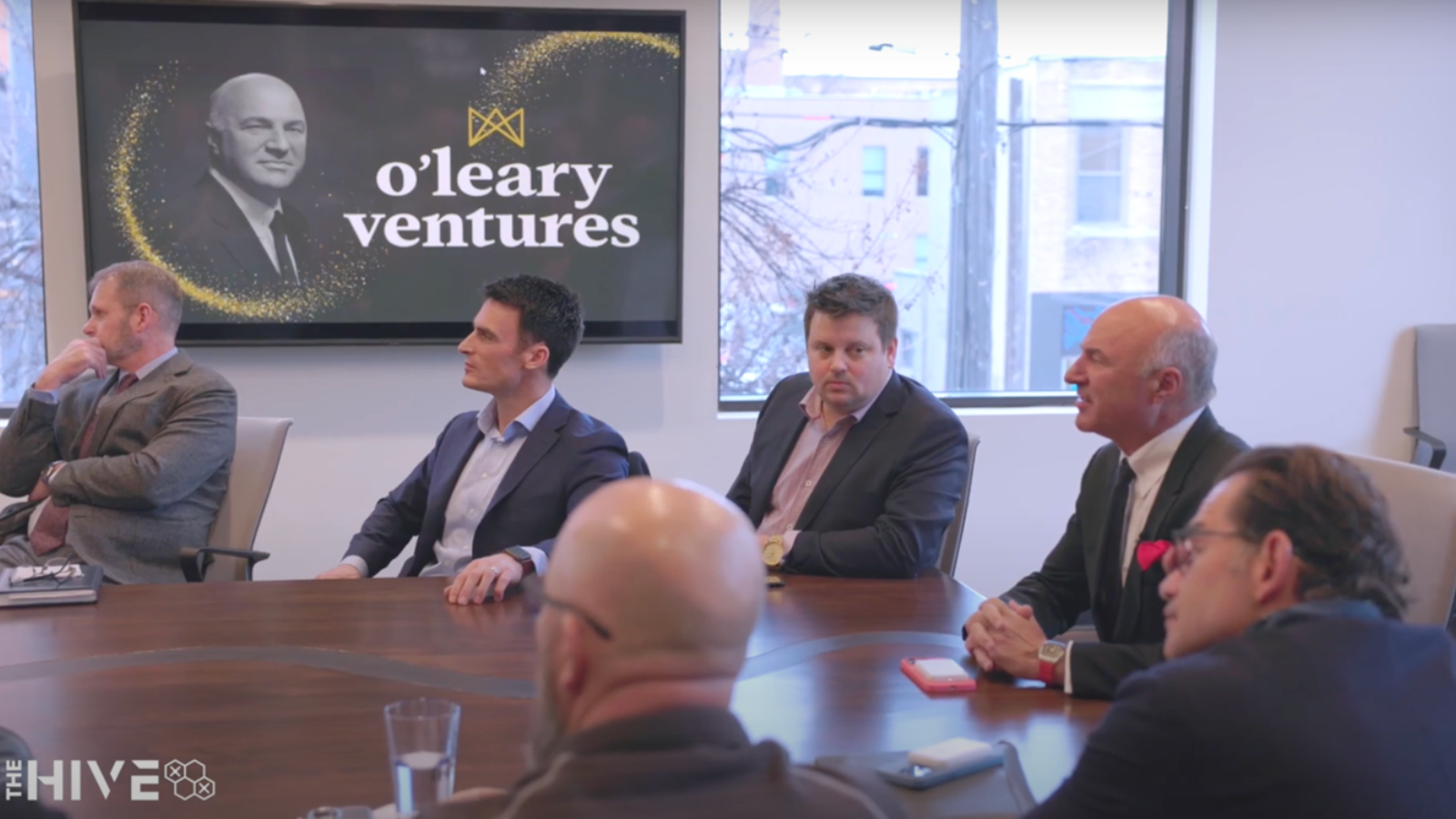 Kevin O'Leary sits in the board room at The Hive alongside Johnny, The Mayor, and Keith Lund, discussing UAS ecosystem in Grand Forks