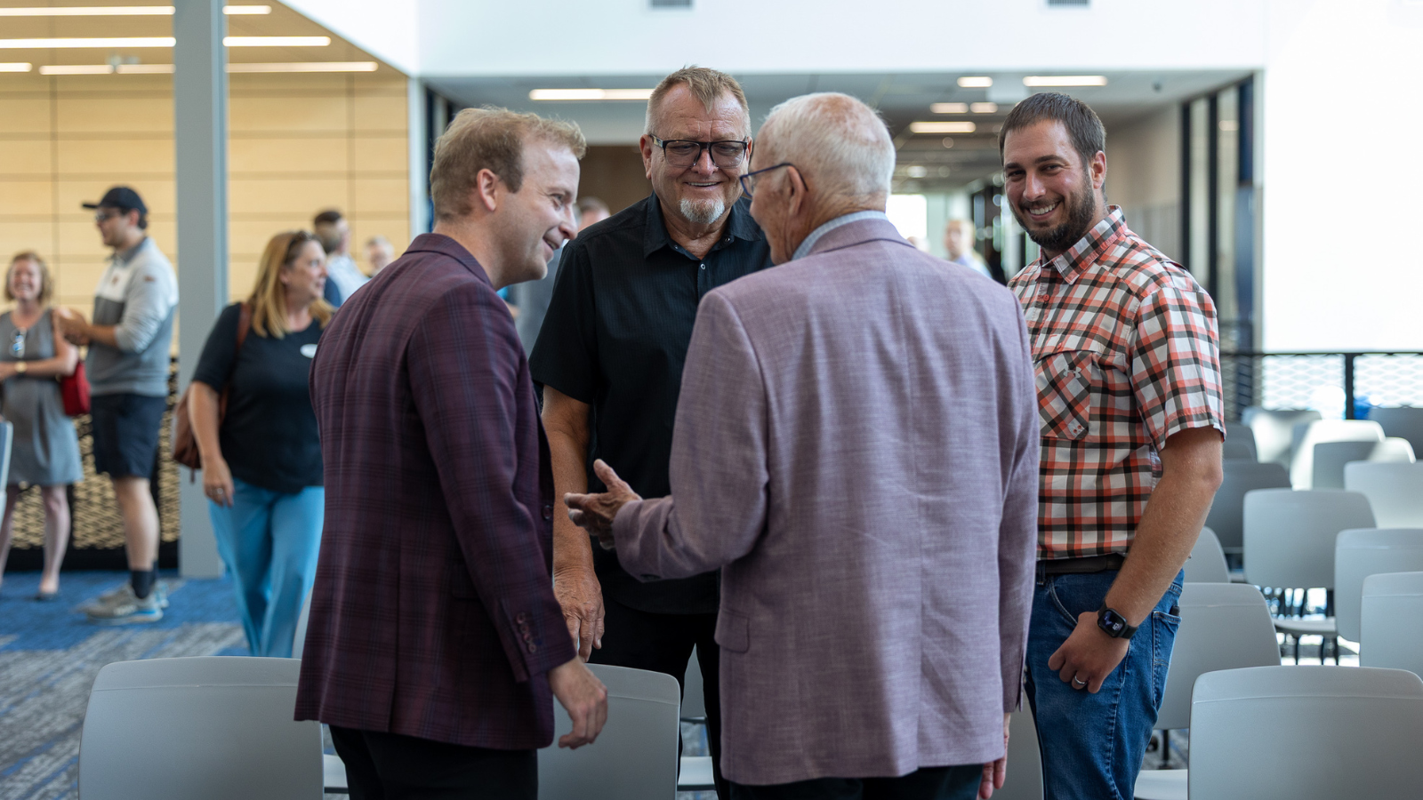 A group of businessmen in varying outfits talk with smiles during the grand opening of the Grand Forks Career Impact Academy
