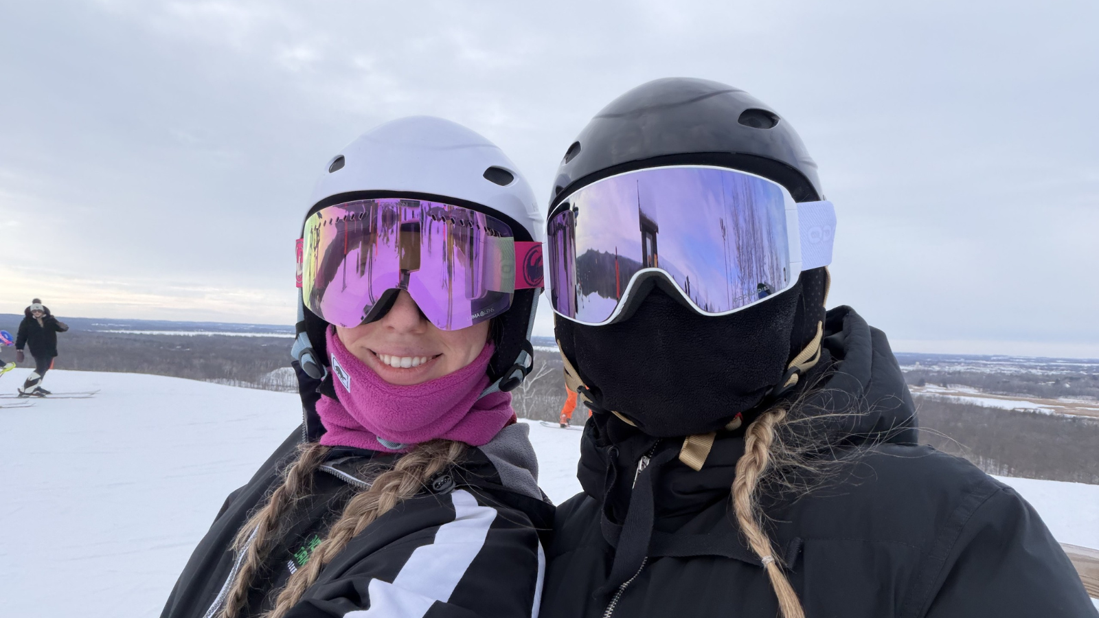 Two women face the camera on the top of Detroit Mountain for a selfie. They have their goggles and masks on with their braids coming out the front.