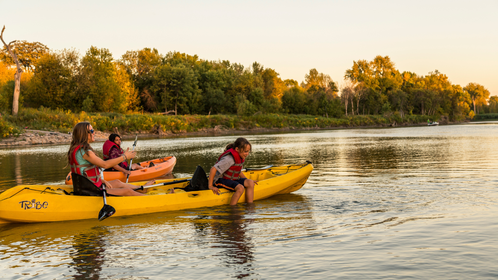 Grand Forks Golden Hour Kayakers A group of kayakers on the Red River in Grand Forks kayak along during golden hour. One kid hangs off the side to dip their feet in the water.