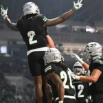 Men's football team celebrates a touchdown in their black uniforms